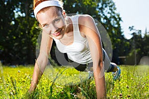 Young woman doing push ups on grass.