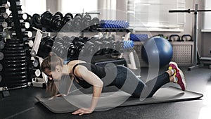 Young woman doing push ups in a gym, side view