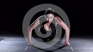 Young woman doing push-ups on her knees in a gym, on black