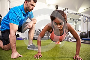 Young woman doing push ups under supervision of a trainer