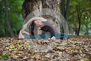 young woman doing revolved seated angle yoga pose outdoors