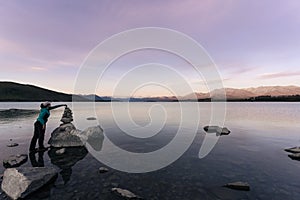 Young woman doing rock balancing in Lake Tekapo, New Zealand