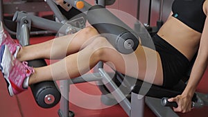Young woman doing seated leg curls in sports club indoors. Attractive athlete prepares legs and buttocks