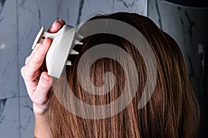 Young woman doing self hair scalp massage with scalp massager for hair growth stimulating at home.