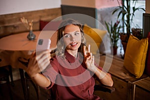 Young woman doing selfie on mobile phone showing victory sign