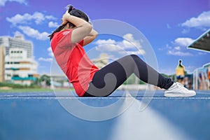 Young woman doing sit-ups exercise on running track before running. Sport and exercise concept