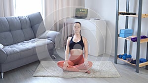 Young woman is doing slow tilt forward in yoga sitting on mat at home.