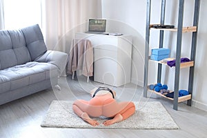 Young woman is doing slow tilt forward in yoga sitting on mat at home.