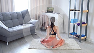 Young woman is doing slow tilt forward in yoga sitting on mat at home.