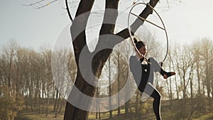 Young woman doing some acrobatic elements on aerial hoop outdoors in slow-mo