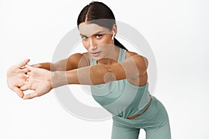 Young woman doing stretch workout and looking confident, listening music in gym, wearing wireless headphones, white