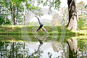 Young woman doing sun salutation yoga practice on grass in park near river