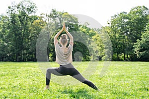 Young woman doing sun salutation yoga practice on green grass loan in sunny park