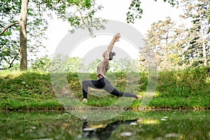 Young woman doing sun salutation yoga practice on green grass loan in sunny park