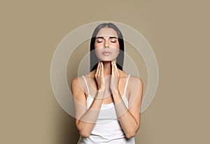 Young woman doing thyroid self examination on beige background