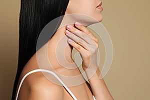 Young woman doing thyroid self examination on beige background, closeup