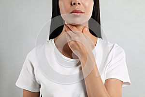 Young woman doing thyroid self examination on light background, closeup