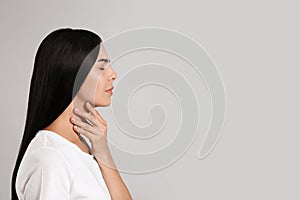 Young woman doing thyroid self examination on light background. Space for text