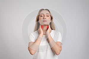 Young woman doing thyroid self examination on light grey background
