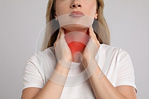 Young woman doing thyroid self examination on light grey background, closeup
