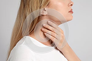 Young woman doing thyroid self examination on light grey background, closeup