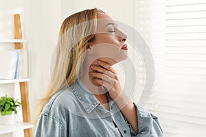 Young woman doing thyroid self examination near window at home