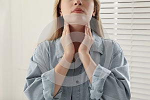 Young woman doing thyroid self examination near window indoors, closeup