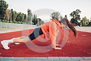 Young woman doing warm-up exercises on sportsground early in the morning