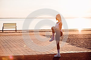 Young woman doing warm-up exercises on sportsground early in the morning