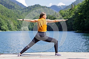 Young woman doing warrior yoga pose near the lake