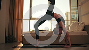 Young woman doing yoga asana bridge pose with right leg up in front the window in living room at home. Performing