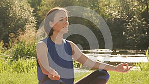 Young woman doing yoga exercise in green park, meditating in summer sunny morning. Meditation, zen, harmony concept. Female practi