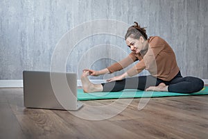 Young woman doing yoga exercise at home watching online yogs class at laptop