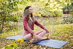 Young woman doing yoga exercise outdoor in the park near lake, sport yoga concept