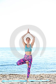 Young woman doing yoga exercises on beach