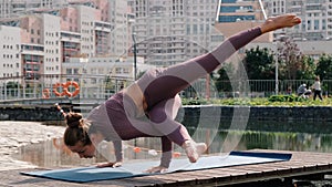 Young woman doing yoga exercises with city on background. eka pada kaundiniasana