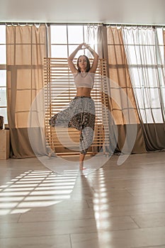 Young woman doing yoga exercises early in the morning. Meditates after sleep in a bright sunny room. Healthy lifestyle