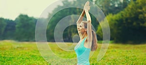 Young woman doing yoga exercises on the grass in summer park