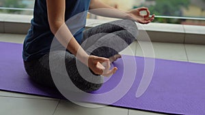 Young woman doing yoga exercises on her balcony in multi-storey building with a view on a downtown with skycrappers