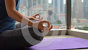 Young woman doing yoga exercises on her balcony in multi-storey building with a view on a downtown with skycrappers