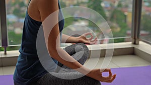 Young woman doing yoga exercises on her balcony in multi-storey building with a view on a downtown with skycrappers