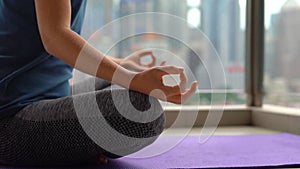 Young woman doing yoga exercises on her balcony in multi-storey building with a view on a downtown with skycrappers