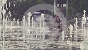 Young woman doing yoga exercises inside the fountain