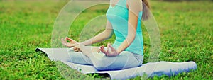 Young woman doing yoga exercises on a mat on the grass in summer park