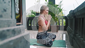 Young woman doing yoga exercises, meditates and prays on yoga mat on veranda