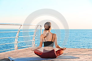 Young woman doing yoga exercises on pier