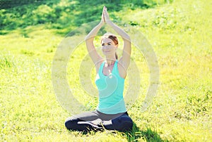 Young woman doing yoga exercises sitting on grass in summer day