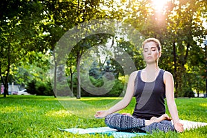 Young woman doing yoga exercises in the summer city park.