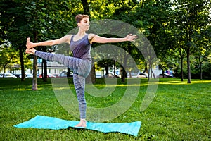 Young woman doing yoga exercises in the summer city park.