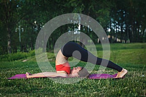 Young woman doing yoga exercises in the summer city park. Health lifestyle concept.